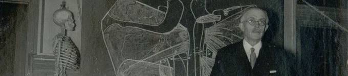 Photographie noir et blanc du Dr Olivier donnant un cours, squelette à gauche et tableau noir en fond
